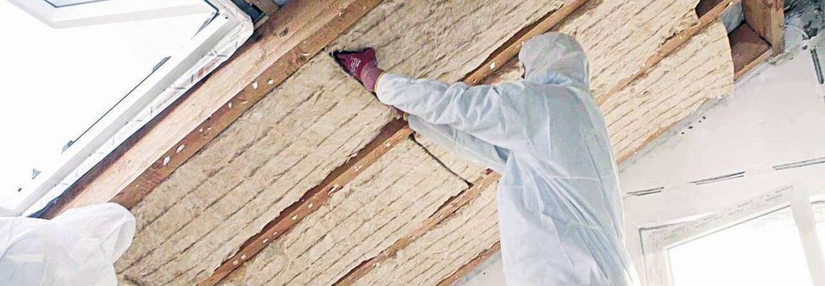 Ein Handwerker bringt die Dachdämmung zwischen den Sparren an.